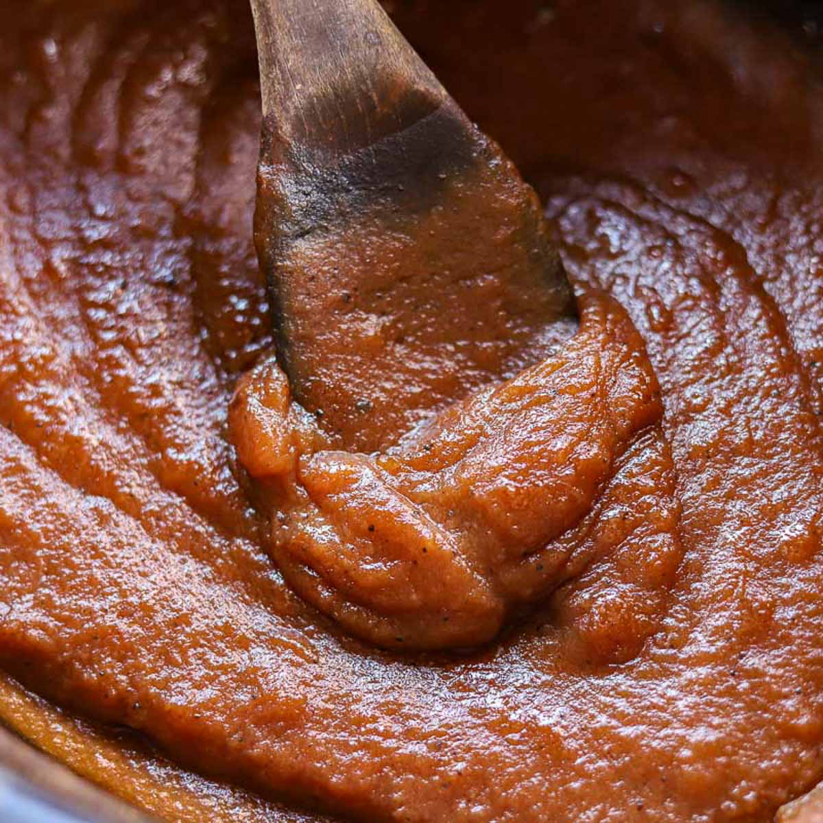 apple butter in the slow cooker with a wooden spoon in the center