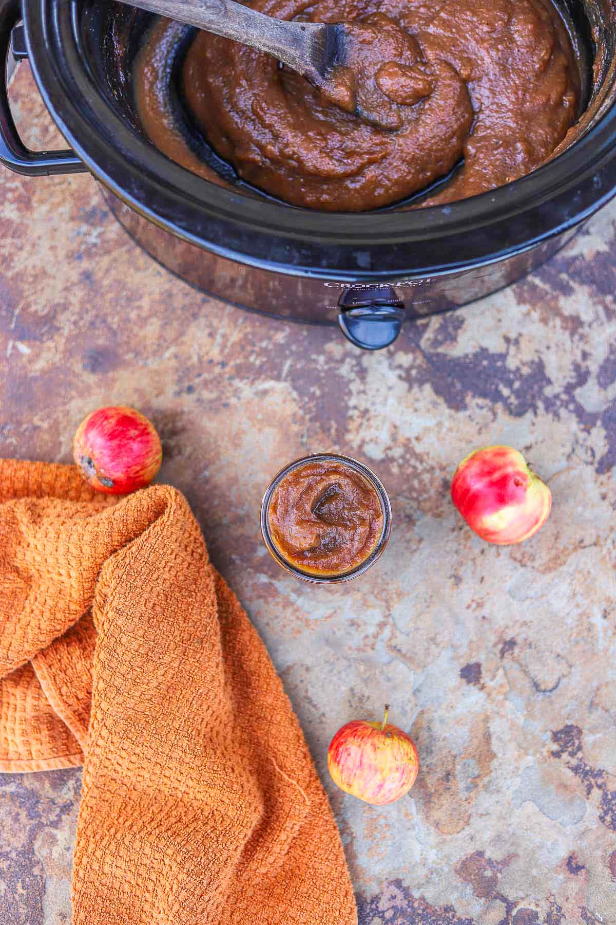 apple butter jar with apples and more apple butter in a slow cooker