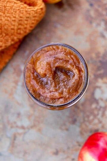 apple butter in a jar with an orange towel and an apple