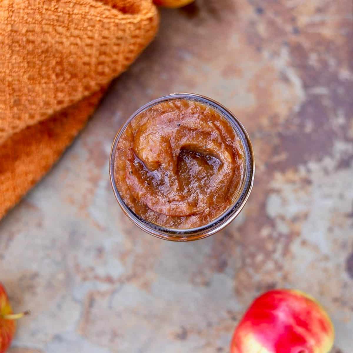 apple butter in a jar with an orange towel and an apple