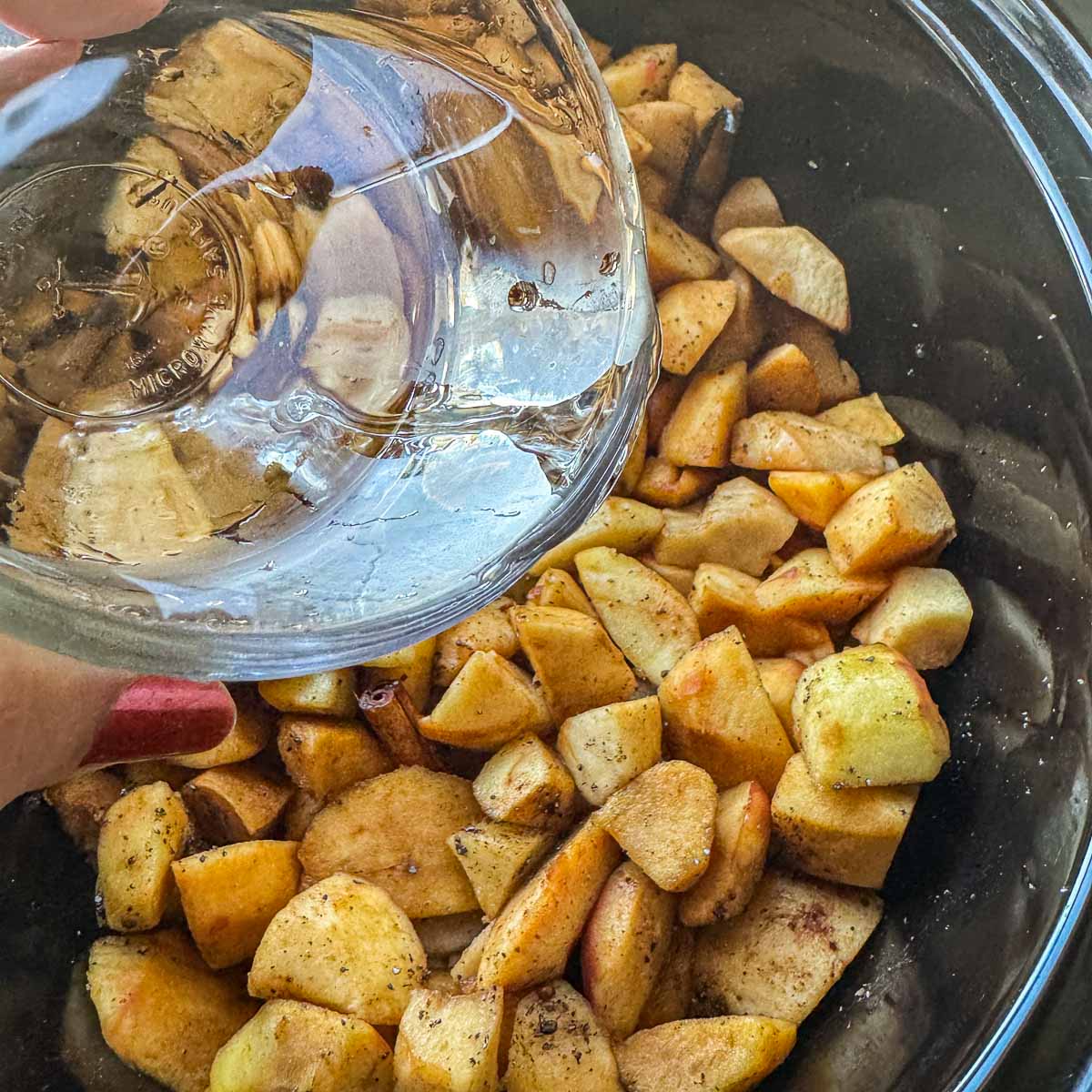 adding water to spiced chopped apples in a slow cooker